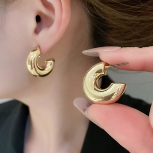 Detail of high-polished gold-toned chunky C-shape hoop earrings with a metallic finish