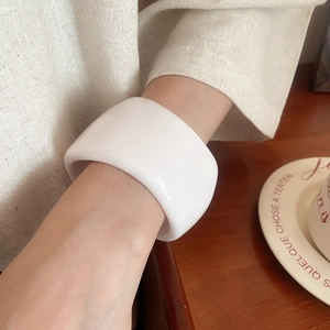 Detail showing a wide irregular glossy white resin bangle worn in a minimalist style