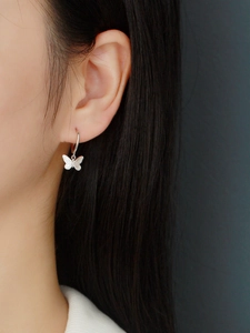 Primer plano de modelo con pendientes de mariposa plateados con acabado metálico liso