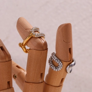 Dettaglio di anelli a C oro e argento con micro-pavé di cristalli su mano in legno
