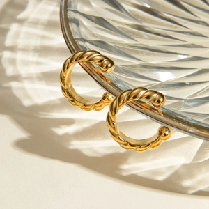 Macro shot of gold stainless steel twisted rope hoop earrings on a textured glass tray