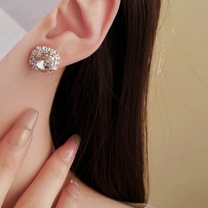 Close-up of elegant square silver stud earring with large centered gem and diamond halo