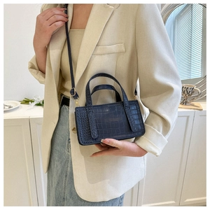 Detail view of a navy blue crocodile embossed leather handbag with twin handles and strap