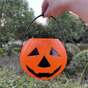 Classic orange Halloween pumpkin candy bucket with black handle held against green plants