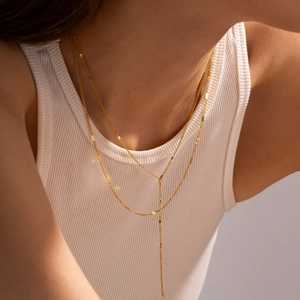 Detail of a layered golden Y-shaped titanium steel necklace on a female model neck