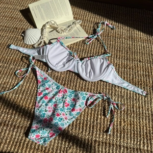 Flachbild des geblümten Bikinisets auf Webmatte mit Urlaubsaccessoires und Muscheln