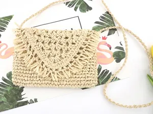 Detail of hand-woven straw crossbody bag with fringe trim on flap and slim braided strap