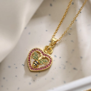 Gold-plated heart necklace with zircon bee and crown charm on white fabric