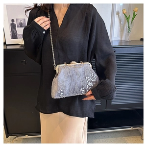 Silver sequin clutch bag with metal chain shown on model in modern home setting