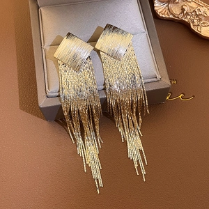 Detailed close-up of golden square tassel earrings with sparkling rhinestones on a jewelry box