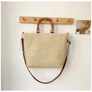 Detailed shot of woven straw handbag featuring a bamboo handle and brown leather strap