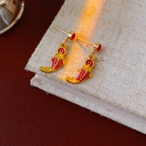 Détail de boucles d'oreilles carpe koï dorées avec émail rouge sur un livre en lin