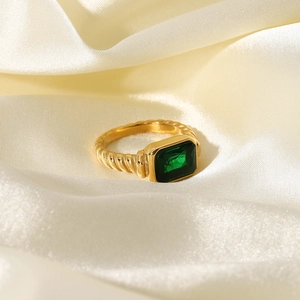 Golden twisted croissant ring with emerald green gemstone on soft beige silk fabric