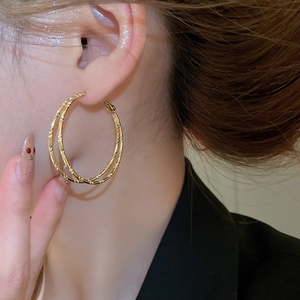 Close-up of golden double-layered bamboo style hoop earrings worn by a model