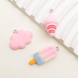 Close-up of pink resin cloud and ice cream charms with metal loops on white surface