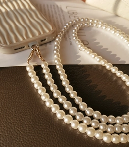 Close-up of white pearl phone lanyard with gold metal clasps on a textured surface