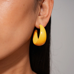 Close-up of a model wearing a thick yellow C-shaped acrylic hoop earring with glossy finish