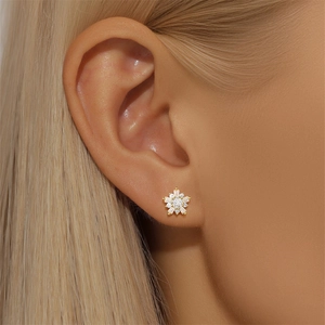 Close-up of a gold floral stud earring with pavé-set crystals on a model's earlobe