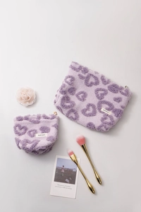 Flat lay of purple plush heart makeup bags with gold brushes and fresh white roses