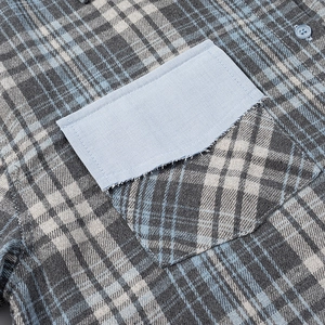 Détail de chemise à carreaux gris avec patchwork bleu effiloché et poche à bouton