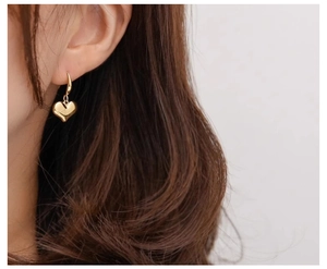 Macro view of polished gold heart-shaped earrings on model highlighting metallic texture