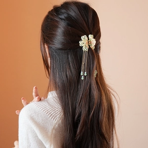 Detail view of a floral hair claw clip with tassels on a model's back-facing hairstyle