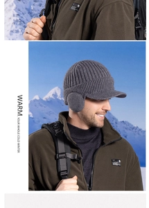 Close-up of gray thermal knitted visor beanie with earflaps in snowy outdoor setting