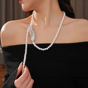 Detail of a pearl necklace with a zircon feather pendant worn on a black sweater