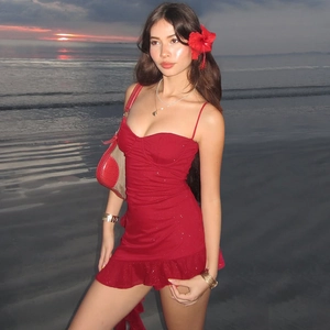 Detail of red sequined dress with ruffled hem and matching floral accessory at beach