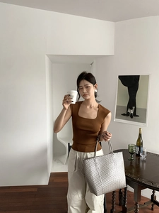 Close-up of a modern silver woven tote bag paired with a brown knit top and beige pants