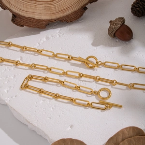 Golden paperclip chain jewelry set with OT toggle clasp displayed on a stone surface