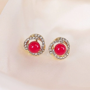 Macro shot of gold pearl earrings with red round beads and sparkling rhinestones inlay
