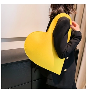 Close-up of bright yellow heart-shaped felt bag held by model in black suit