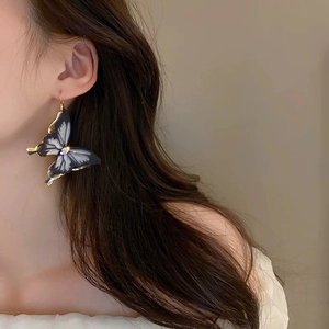 Close-up of a model wearing large dark grey gradient butterfly earrings with tassels