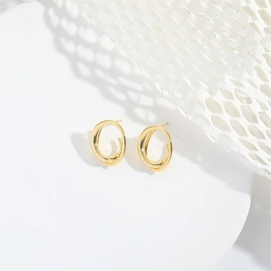 Detailed view of gold twisted oval earrings on minimalist white honeycomb paper background
