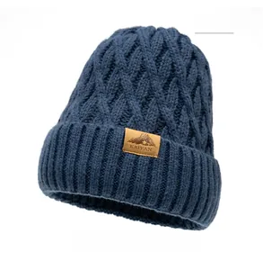 Close-up of thick navy blue cable knit beanie featuring a brown leather embossed logo patch