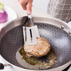 Stainless steel slotted spatula tongs flipping a steak in a frying pan for BBQ and kitchen