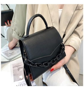 Detail of black PU leather handbag featuring a thick tonal chain and magnetic flap closure