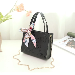 Detail of black marble textured handbag featuring a floral silk scarf and gold chain strap