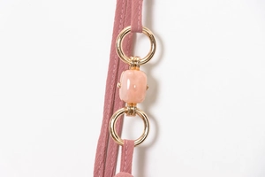 Detail of pink woven strap with gold metal rings and glossy bead on the dress