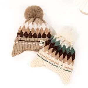 Detail of jacquard knit earflap hat with pompom and M letter patch in beige and camel tones