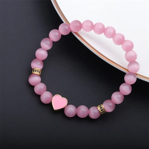 Detailed macro view of pink cat eye stone beads with a heart charm on a beaded bracelet