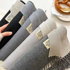 Detail shot of folded scarves in grey and beige tones with soft herringbone knit texture