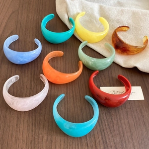 Close-up of colorful resin open cuffs in blue, green, and orange on wood surface