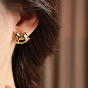 Detail of a golden rocking horse stud earring worn on ear with zircon accents