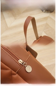 Details einer braunen Ledertasche mit breitem Tragegriff und hellgoldem Metallreißverschluss