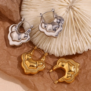 Close-up of dual-layer wavy gold and silver hollow hoop earrings on textured background