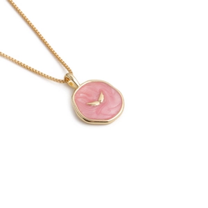 Close-up of gold-plated necklace with pink enamel circular pendant and wing detail