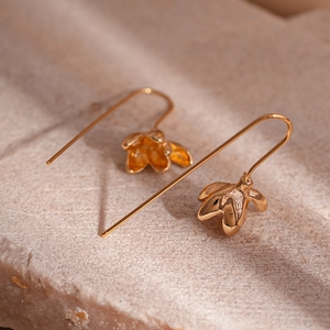 Gros plan de boucles d'oreilles muguet dorées sur un socle en pierre minimaliste