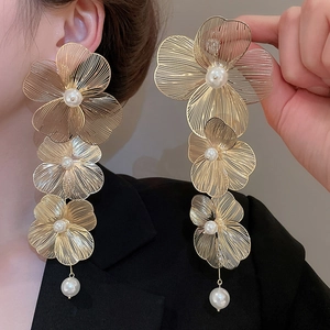 Dettaglio di orecchini a fiore dorati con petali di metallo e perle bianche eleganti